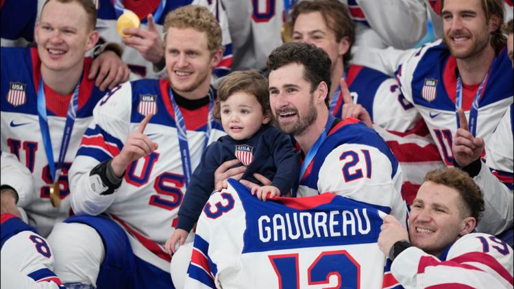 Dylan Larkin holds Johnny, the son of the late player Johnny Gaudreau, while posing with teammates after the men's hockey gold medal game in Italy.