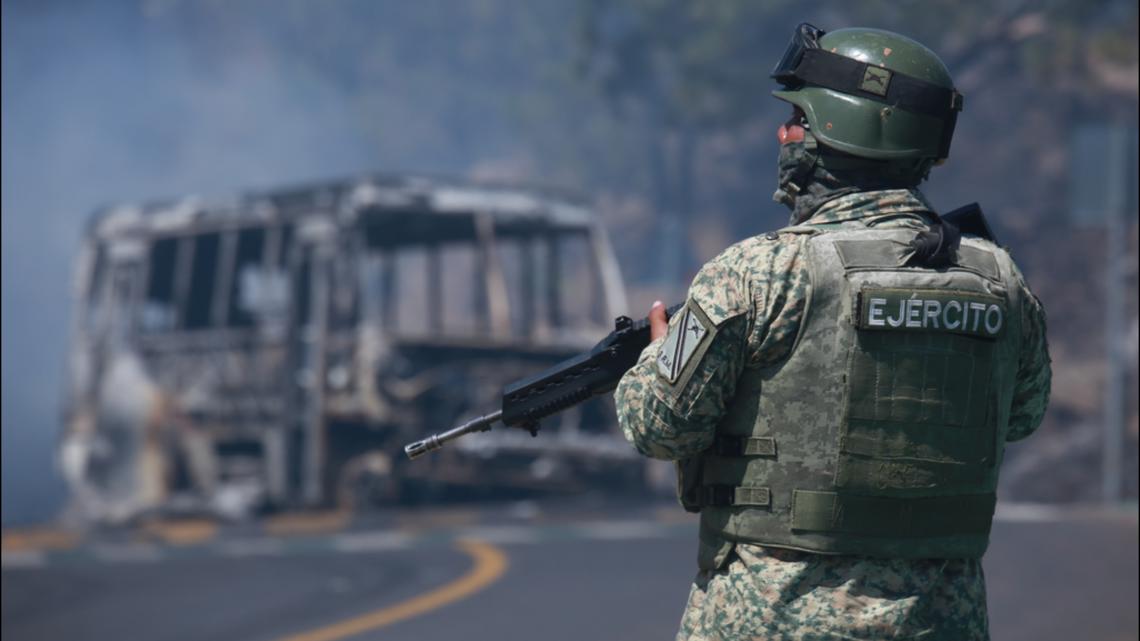 A soldier stands guard by a charred vehicle after it was set on fire in Cointzio, Michoacán state, Mexico, Sunday, Feb. 22, 2026.