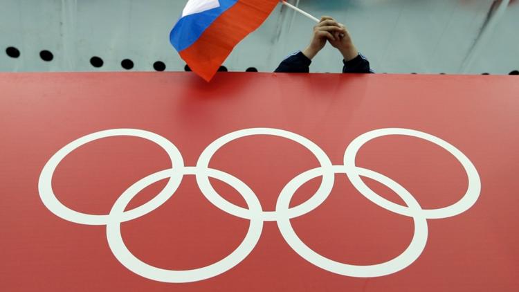 FILE - A Russian flag is held above the Olympic Rings at Adler Arena Skating Center during the Winter Olympics in Sochi, Russia on Feb. 18, 2014.