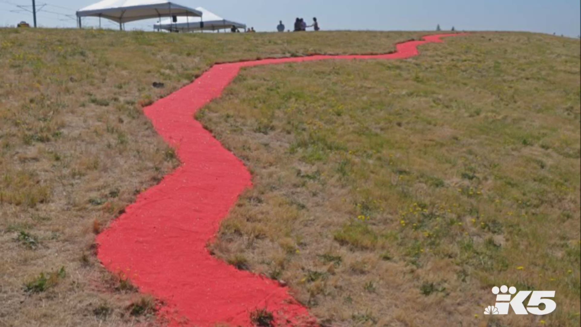 “Red Sand Project: US-MX” is a 350-foot-long red sand path pathway at Sea-Tac Airport that replicates the U.S.-Mexico border and aims to draw attention to human trafficking.